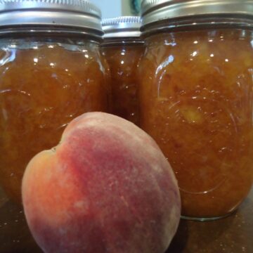 Homemade Peach Butter in clear jars with a peach sitting in front of it