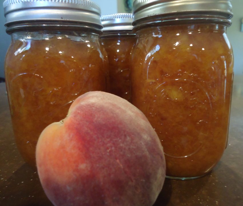 Homemade Peach Butter in clear jars with a peach sitting in front of it