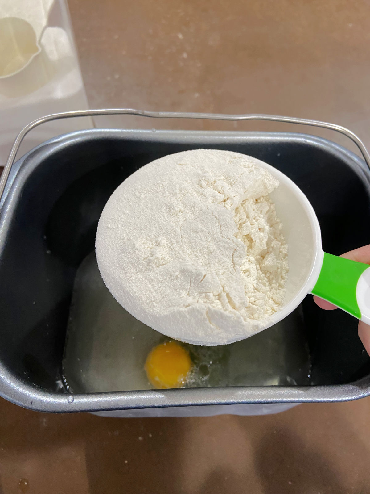 flour being added to a bread machine pan. 