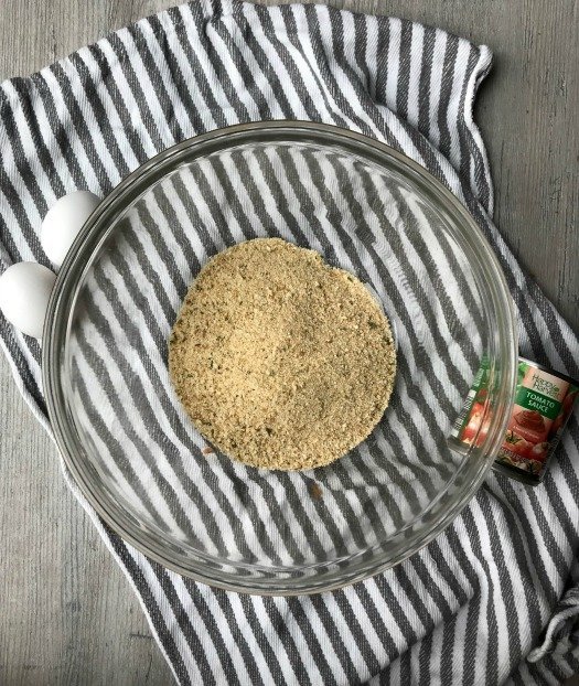 Bread crumbs in a bowl with eggs and tomato sauce on the side