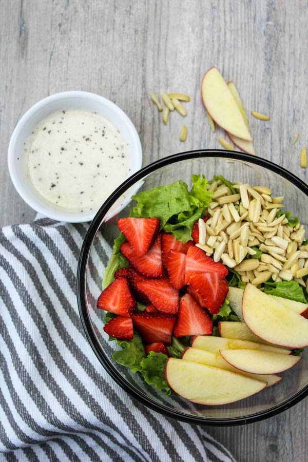 Salad in a clear bowl with honey dressing in a white bowl