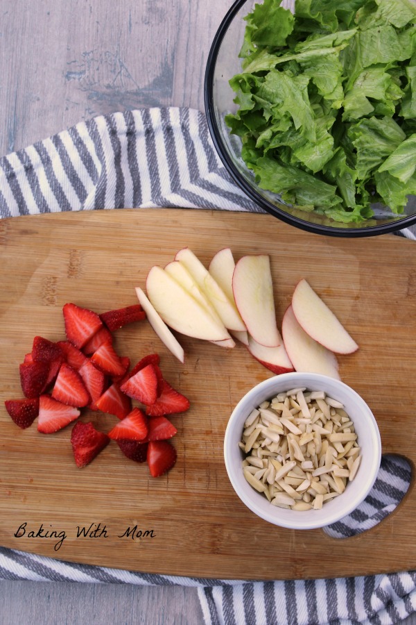 Strawberries, apples and almonds on a cutting board with a bowl of lettuce on the side