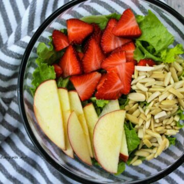 Apples, Strawberries and almonds in a clear bowl on a bed of lettuce