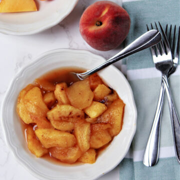 peaches in a white bowl with forks laying nearby.