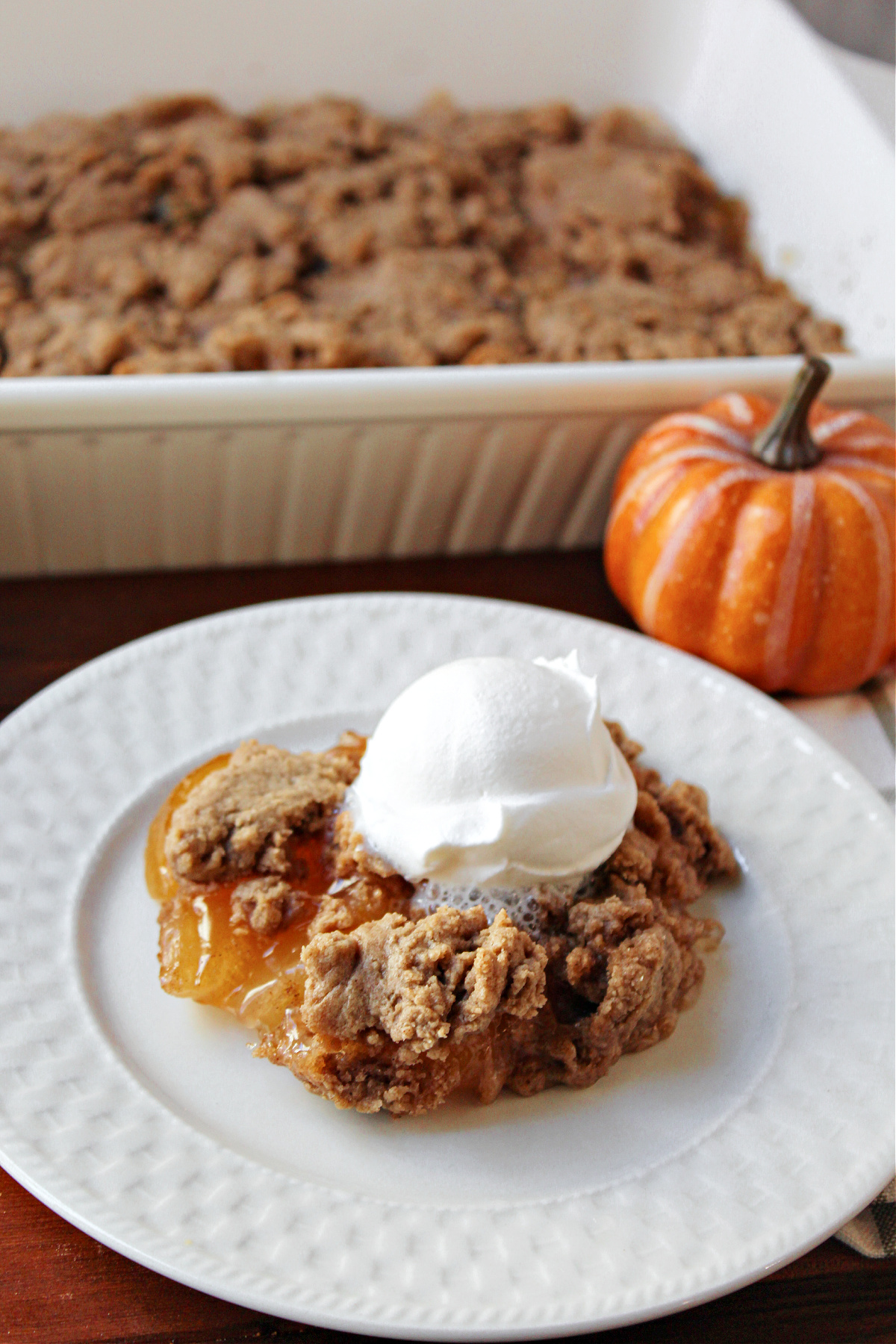 apple spice dump cake on a white plate with whipped cream on top. 