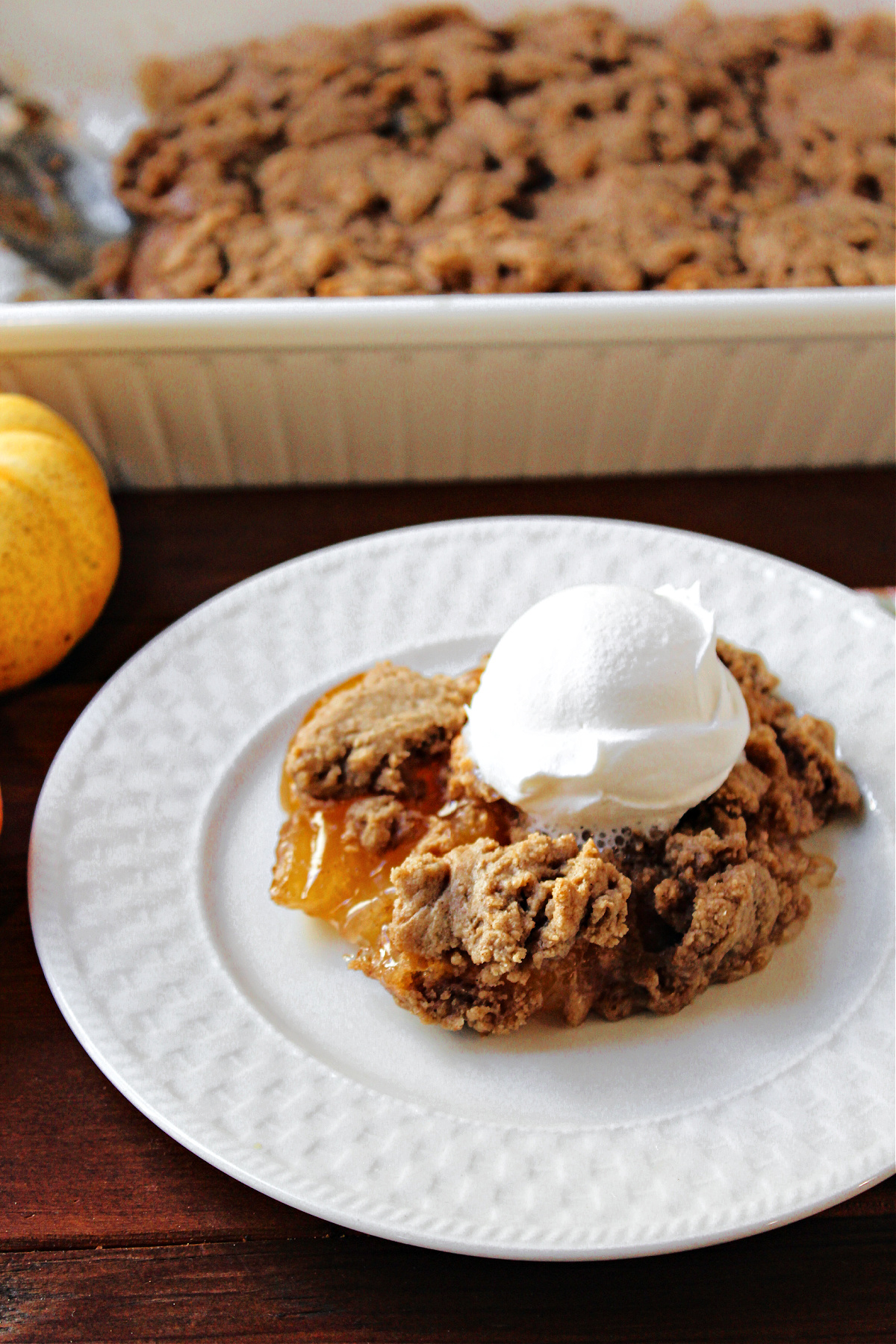 apple spice dump cake on a white plate with whipped cream on top. 