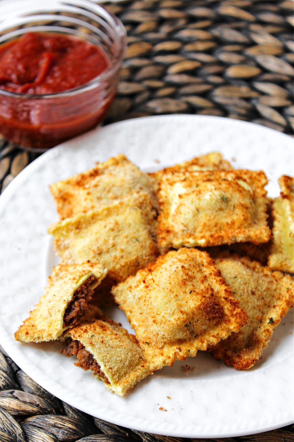 air fryer ravioli on a white plate with sauce behind.
