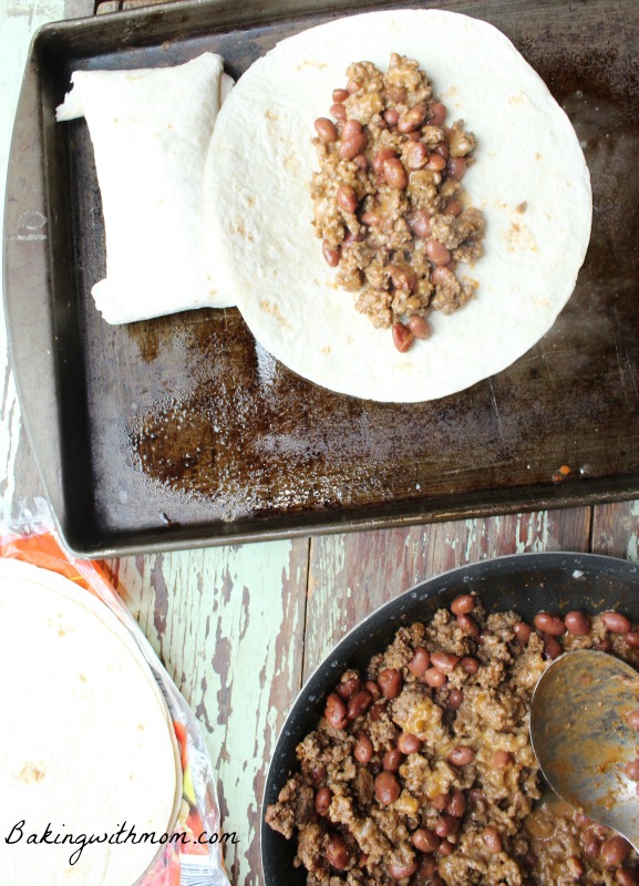 burrito mix in a frying pan and a burrito on a baking sheet. 