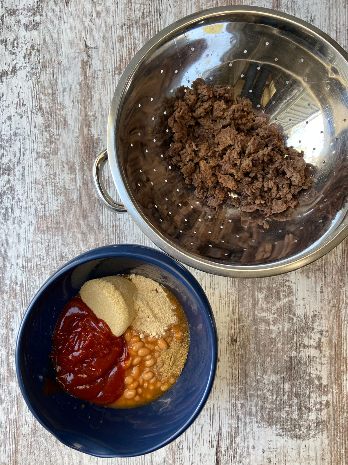 Baked beans in a bowl with hamburger besides. 