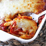 baked mostaccioli casserole in a white casserole dish with a spoon.