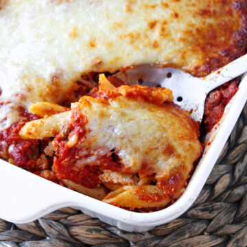 baked mostaccioli casserole in a white casserole dish with a spoon.
