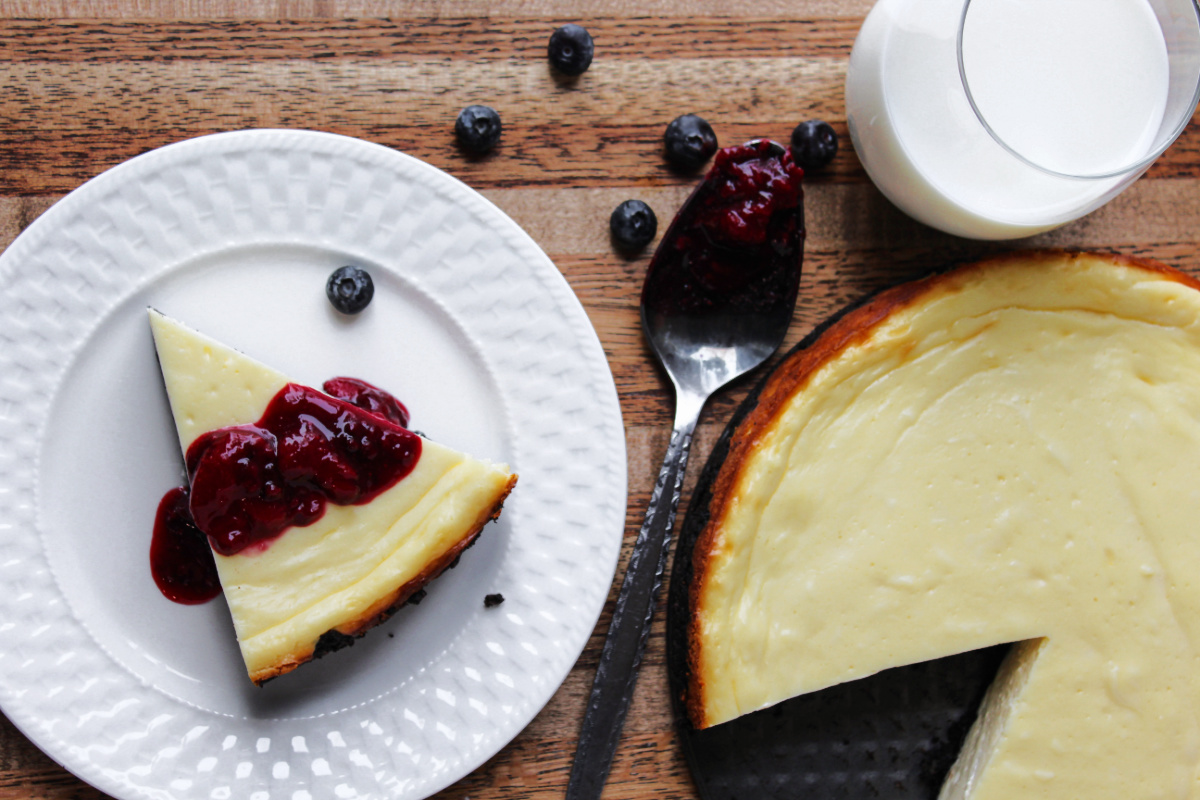 berry cheesecake on a white plate with a large cheesecake besides. 