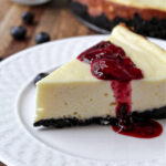 Mixed berry cheesecake on a white plate with blueberries besides.
