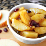 Fried apples in a white bowl with apples besides.