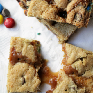 cookie bars with caramel and M&M's and chocolate chips laying besides