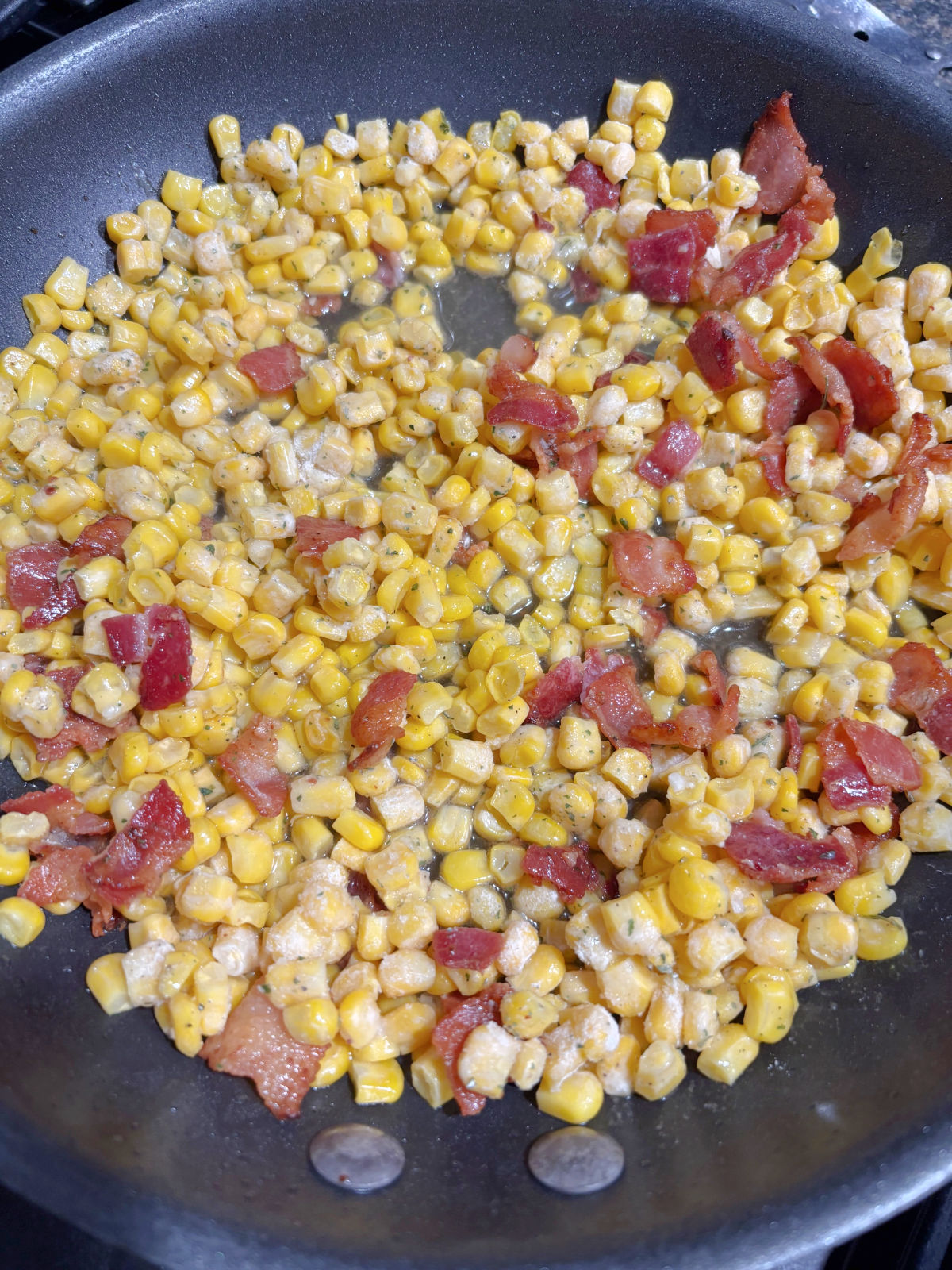 corn and bacon cooking in a frying pan.