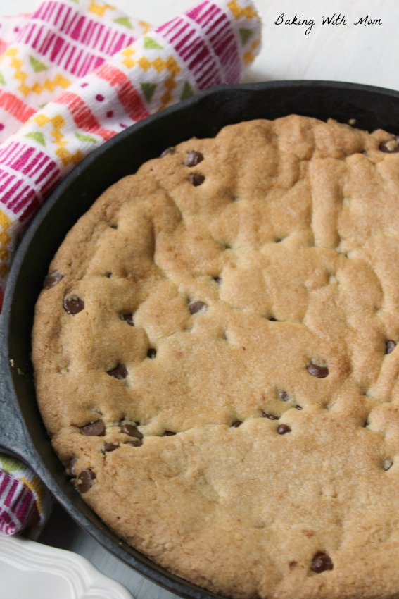Caramel Chocolate Chip Skillet Cookie in a cast iron pan with a multicolored towel nearby