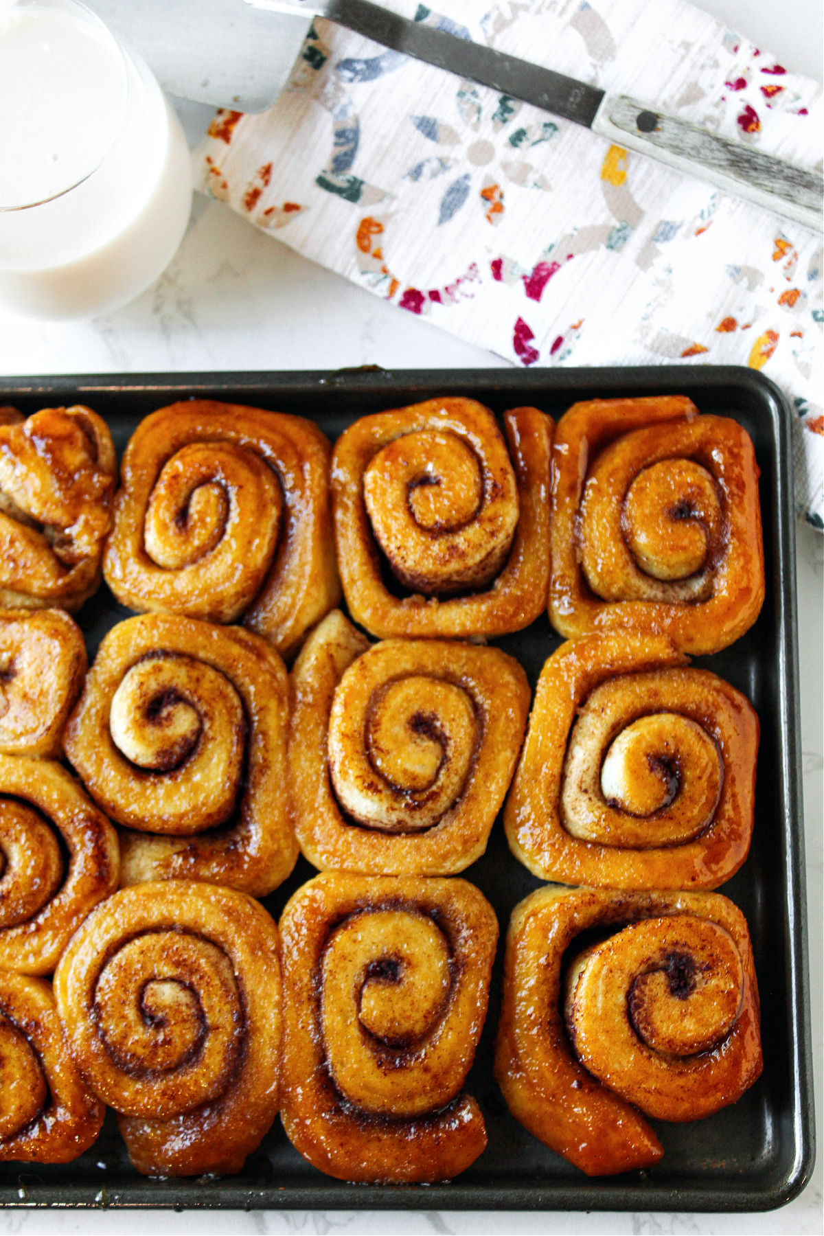 Brown sugar cinnamon rolls on a pan with milk and a spatula.