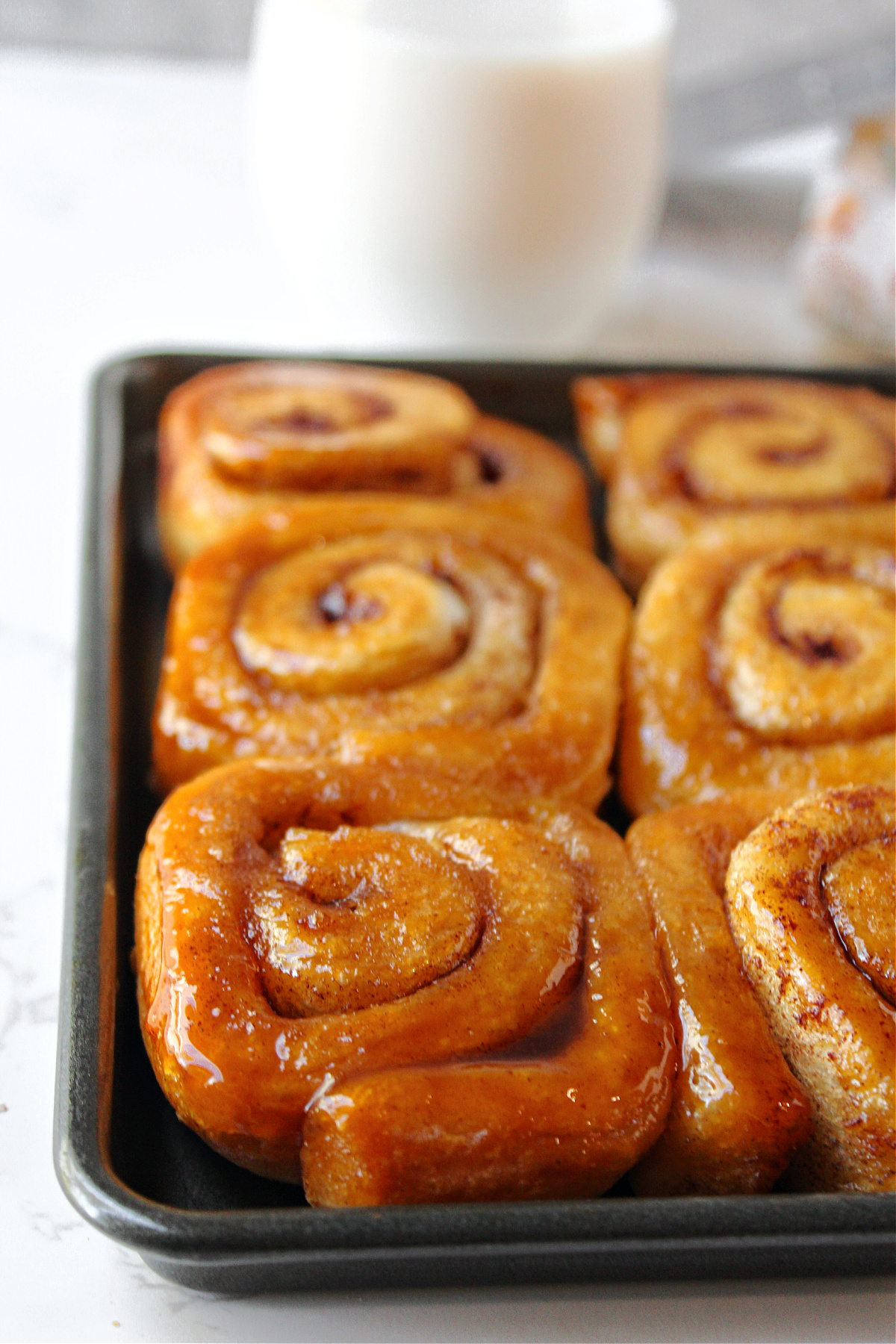Caramel rolls on a pan with milk behind.