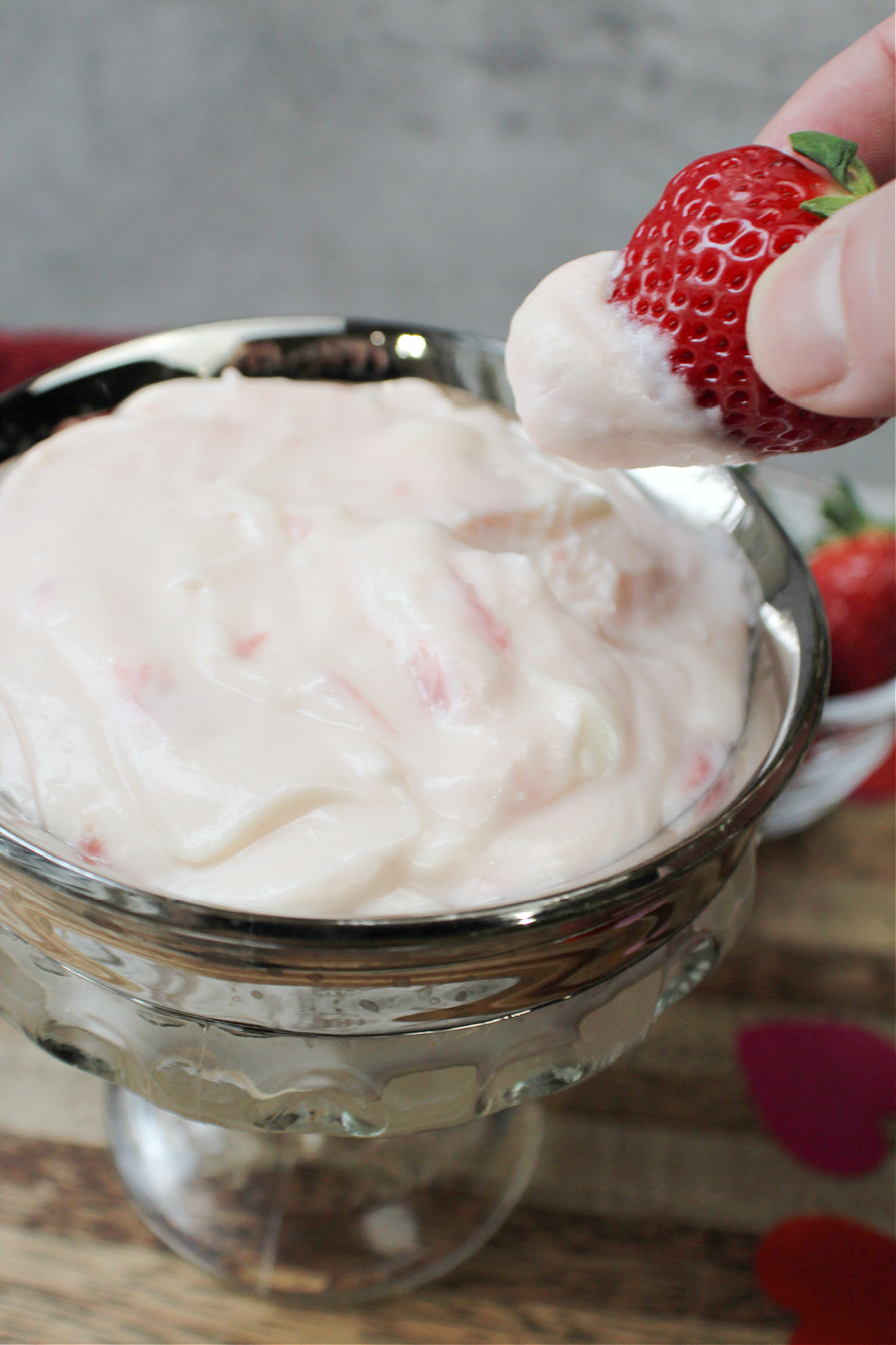 Strawberry dip with a strawberry being held by a hand. 