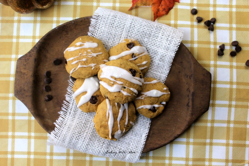 Brown wooden plate with pumpkin cookies on top and chocolate chips scattered besides. 