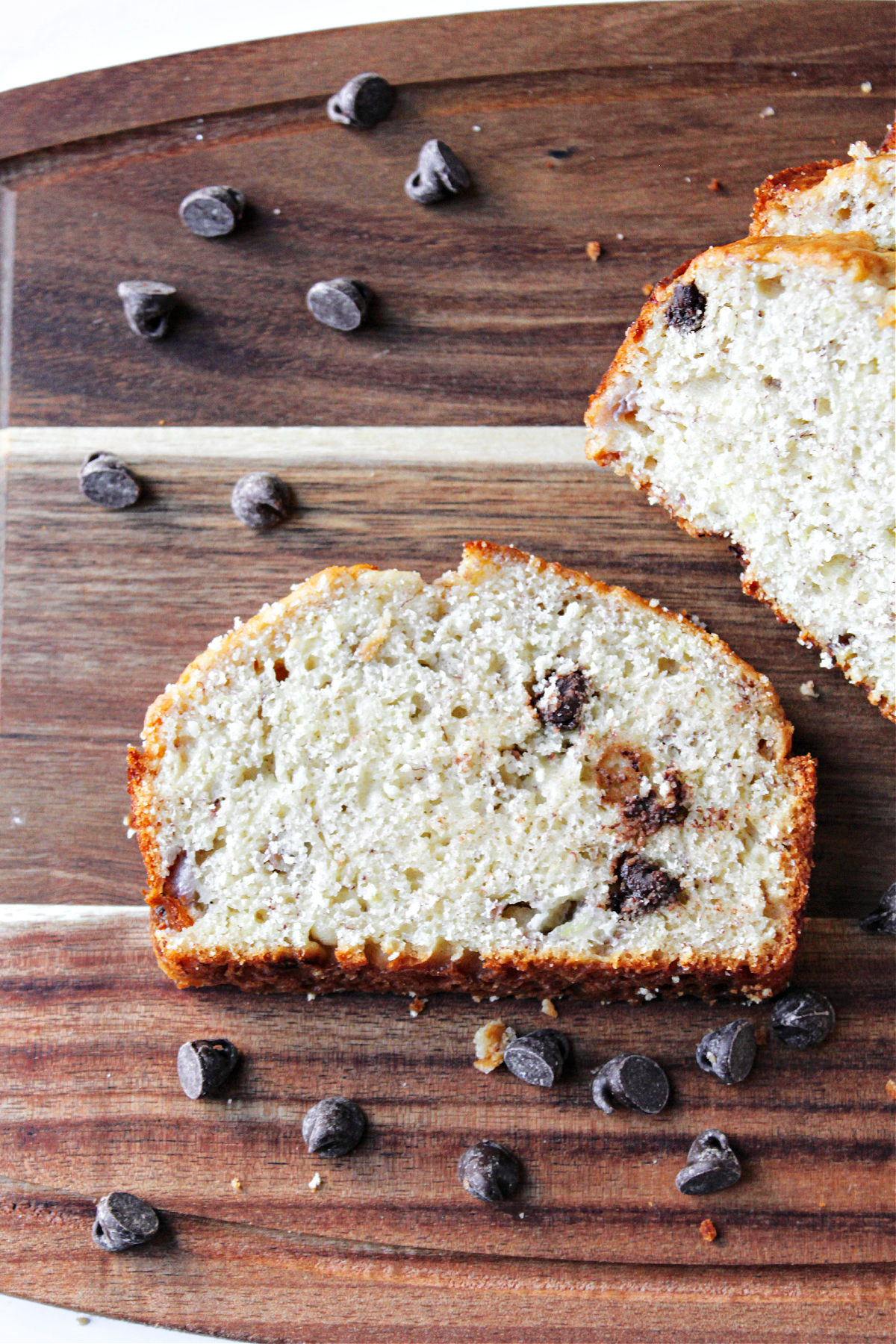 banana bread on a brown board with chocolate chips besides.
