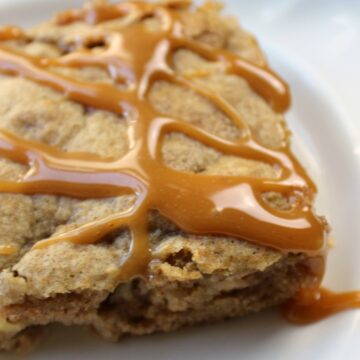 piece of cake with apples and caramel drizzle on a white plate