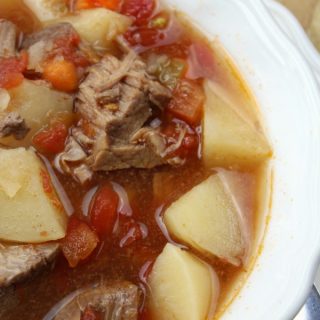 Crock Pot Vegetable Beef Soup in a white bowl with tomatoes, beef and potatoes