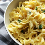 Cheesy buttered noodles in a white bowl with a towel underneath.