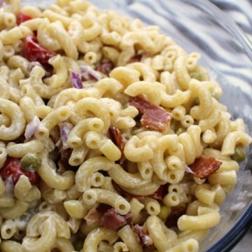 Macaroni salad in a clear bowl with bacon and tomatoes