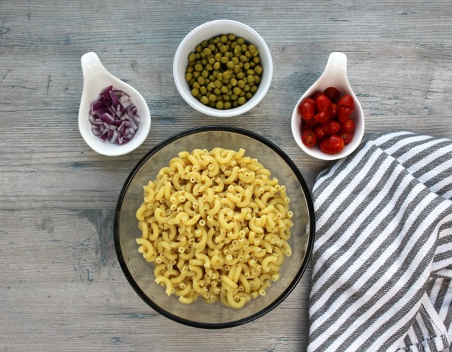 A bowl of macaroni noodles, peas, tomatoes and onions