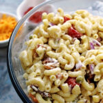 macaroni salad in a clear bowl with ingredients behind.
