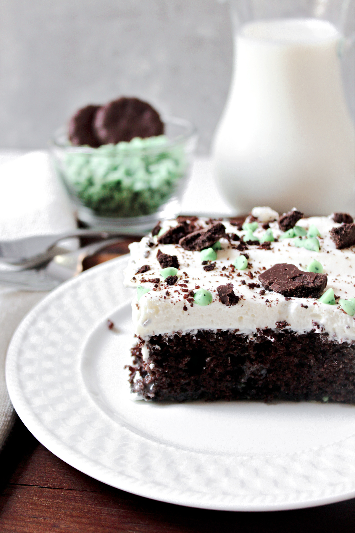 grasshopper poke cake on a white plate with mint chips behind. 