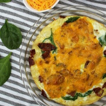 Bacon Spinach Quiche in a clear pie pan with cheese and spinach leaves on the side