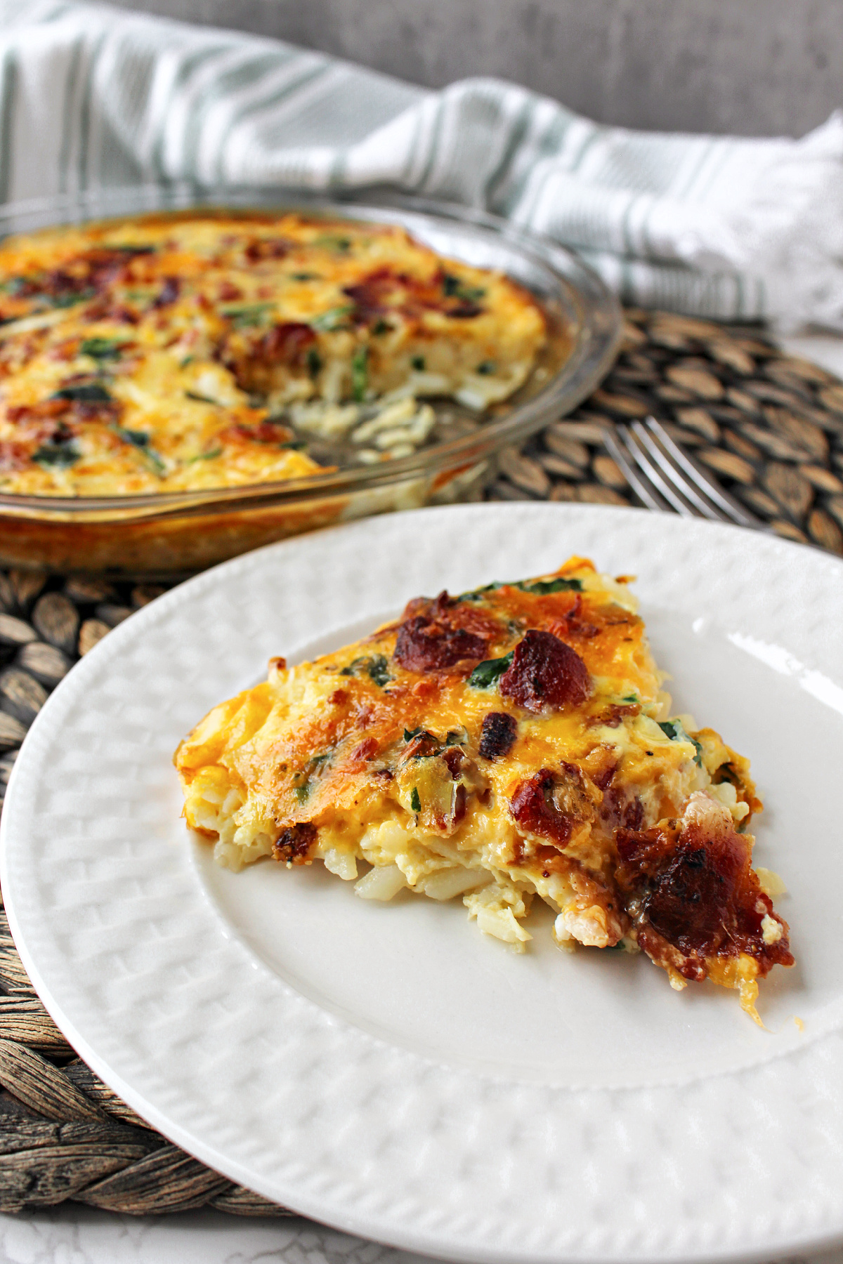 piece of bacon spinach quiche on a white plate.