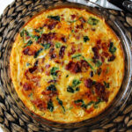 bacon spinach quiche in a pie pan on a brown mat.