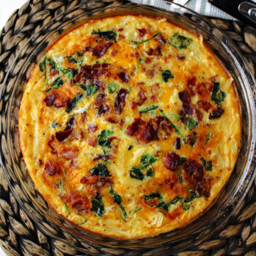 bacon spinach quiche in a pie pan on a brown mat.