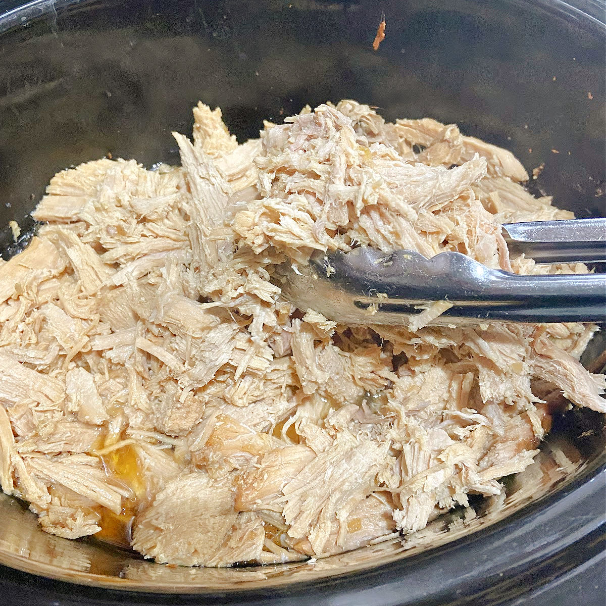 pulled pork with tongs in a crock pot.