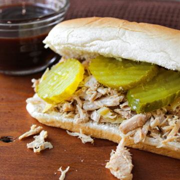 pulled pork on a brown cutting board with pickles.