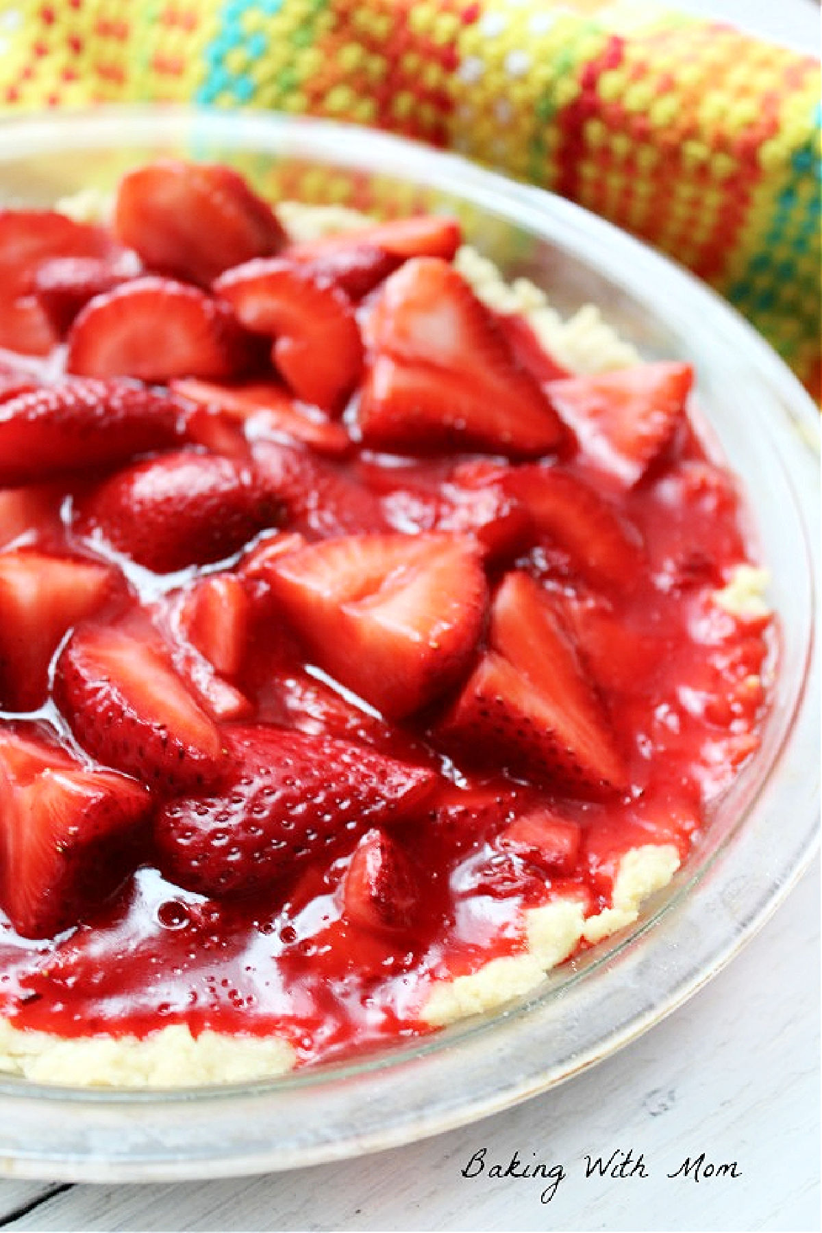 Strawberry pie in a pie pan with a colored towel behind.