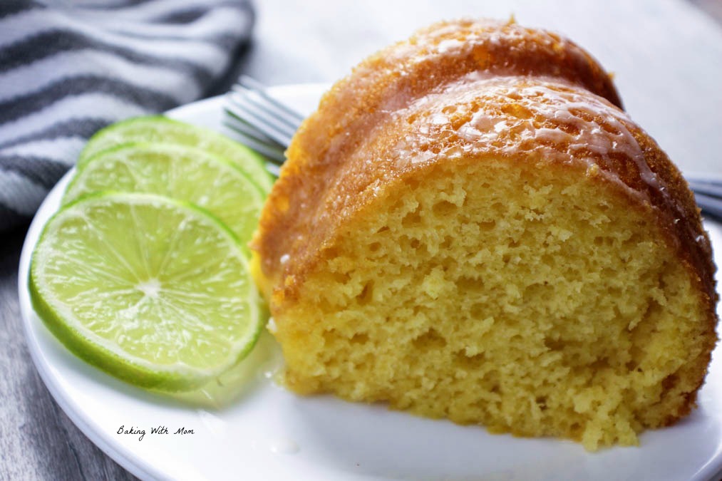 Piece of key lime cake on a white plate with sliced limes