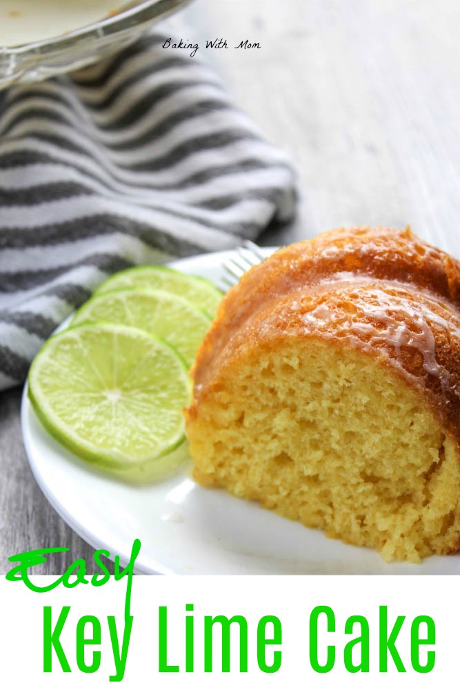 Key lime cake slice on a white plate with a striped towel and lime slices