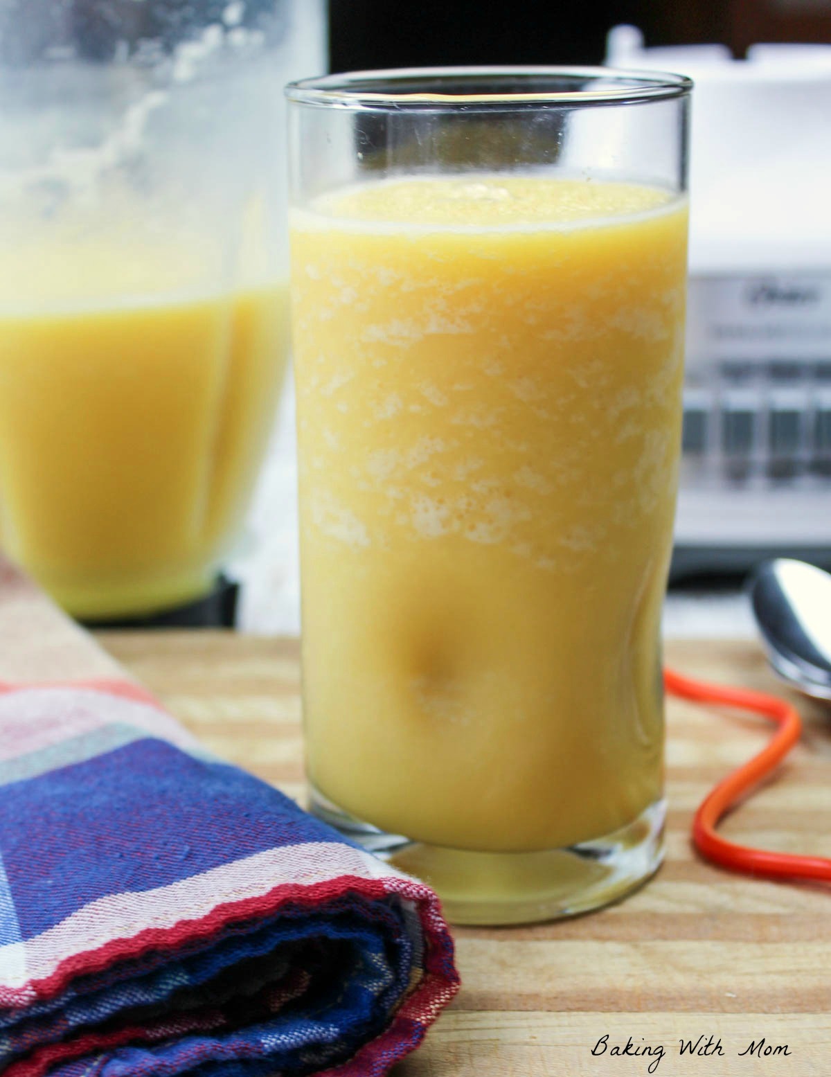 Glass of homemade orange julius with a blender in the background on a wooden cutting board