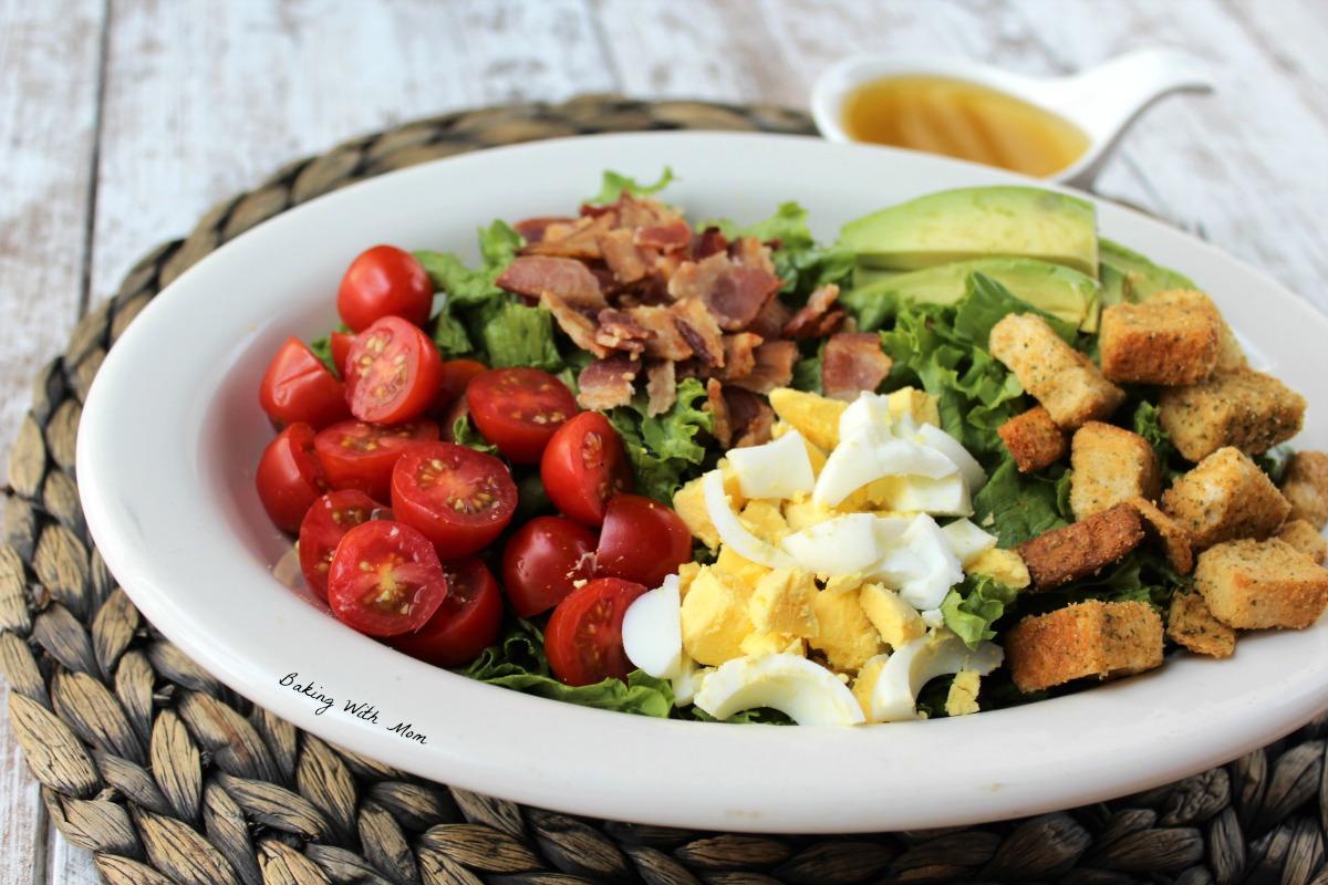 lettuce salad in a white bowl with tomatoes, hard boiled eggs, bacon, slices of avocado and croutons