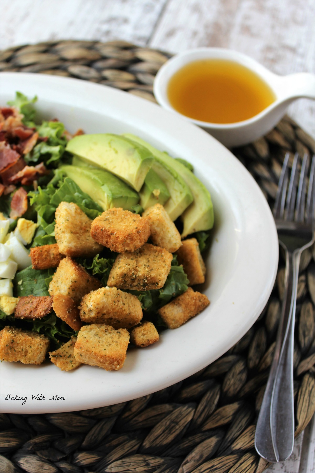 Lettuce salad on a white plate with a fork laying besides. Croutons and avocado on top of salad