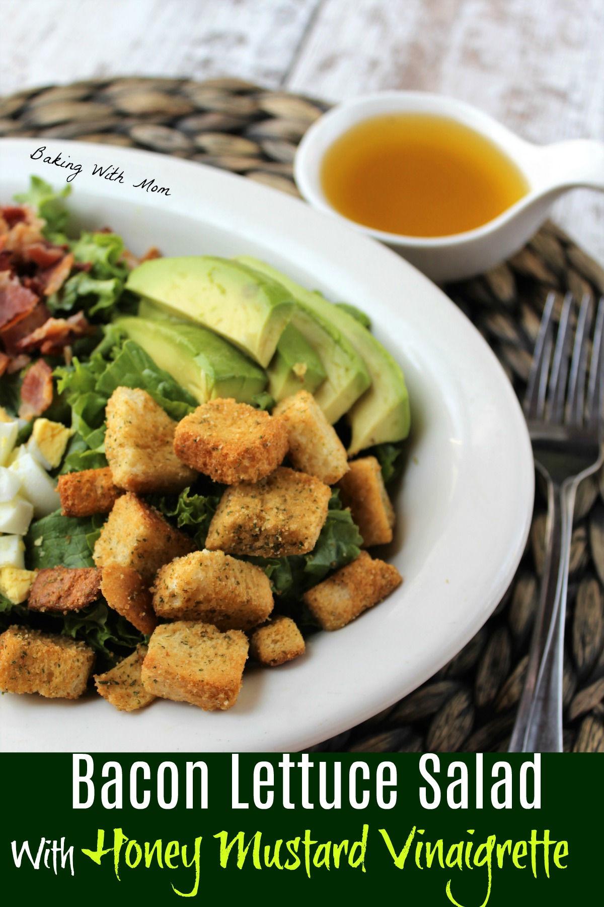 Lettuce salad in a white bowl with Honey Mustard Dressing besides. Lettuce topped with avocado, bacon, croutons, eggs