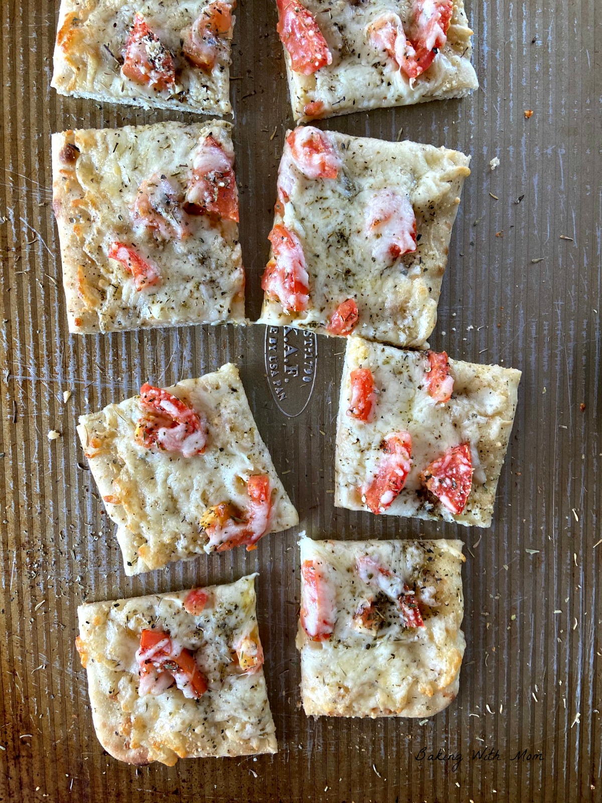 Pieces of flatbread on a baking sheet with tomato, cheese and spices