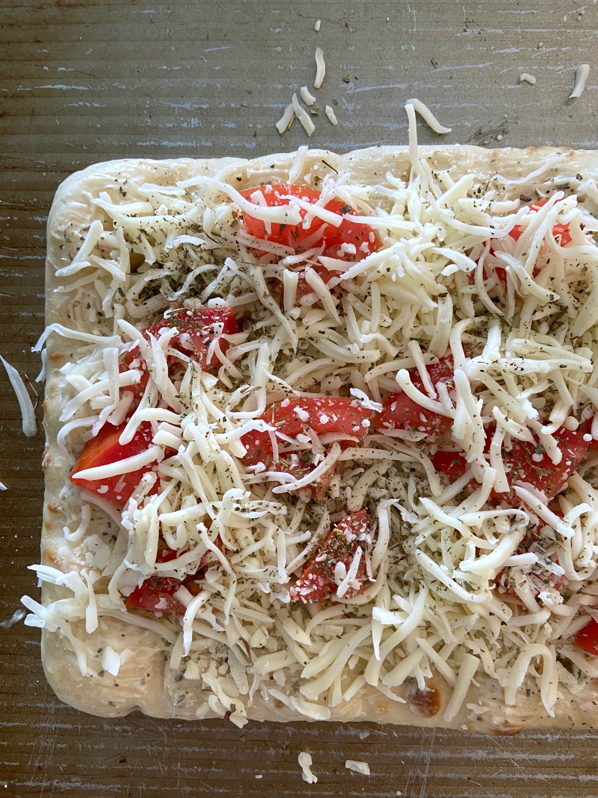 Flatbread topped with shredded cheese, sliced tomatoes and spices on a baking sheet