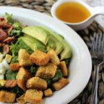 lettuce salad in a white bowl with avocados, croutons, bacon