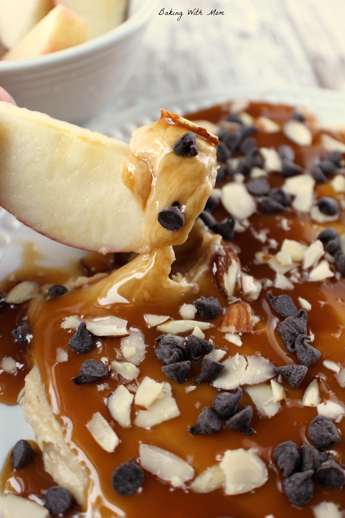 Caramel apple dip with an apple slice, chocolate chips and almonds on a white plate